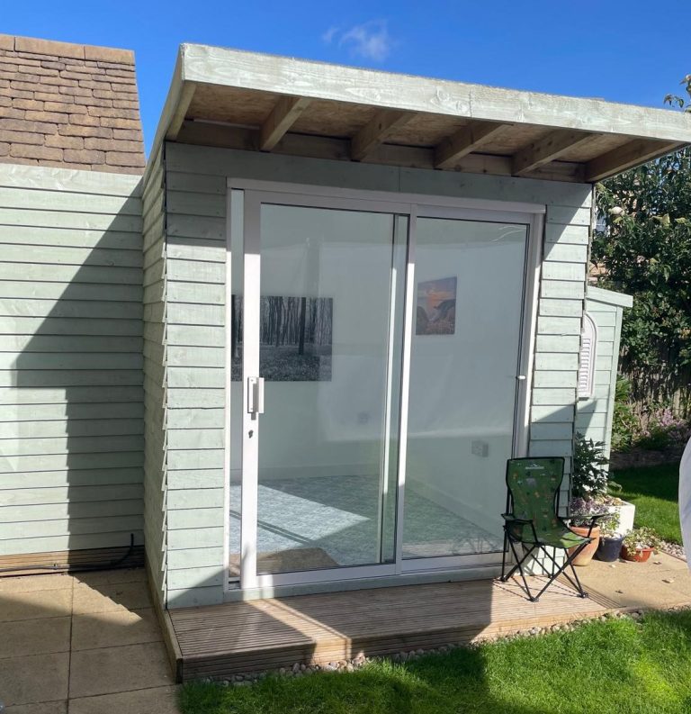 Custom Built Summer House A light coloured exterior summer house with sliding glass doors and space to sit at the front.